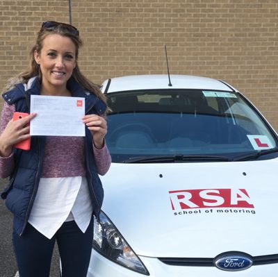 Learner holding her pass certificate beside a white RSA School of Motoring car