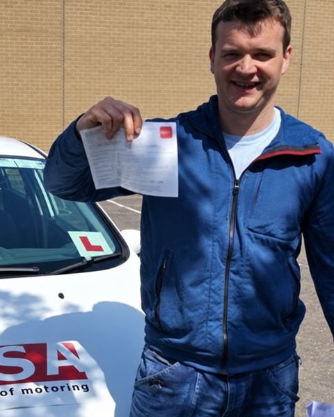 Learner holding his pass certificate beside an RSA School of Motoring car
